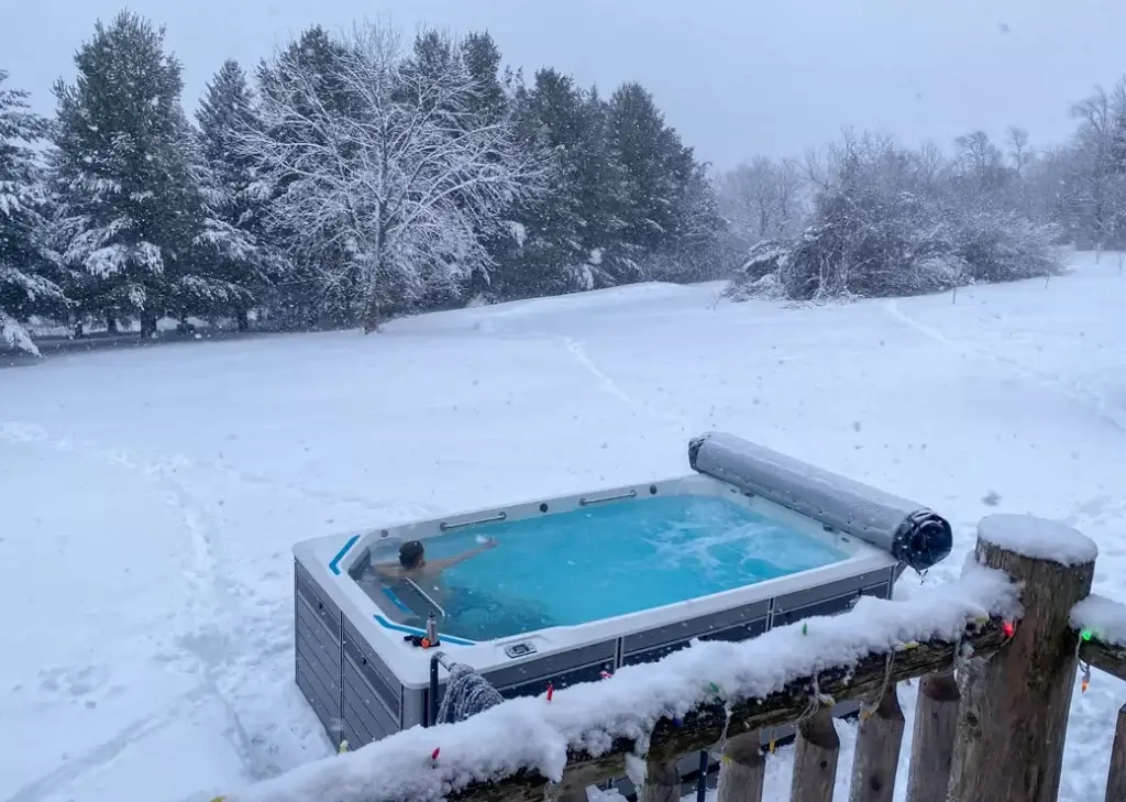 Guy swimming in his swim spa in a backyard covered in snow