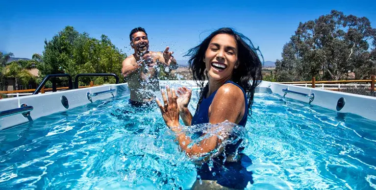 Guy splashing girl while playing in bright blue swim spa water